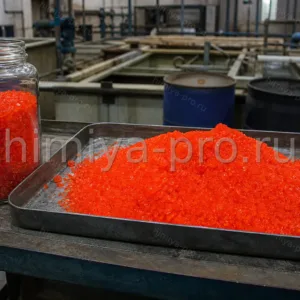 Оранжево-красные кристаллы калия двухромовокислого технического в банке и на поддоне для металлообработки и аналитики.