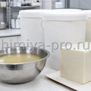 Кремовый фильтрованный баттер ши в ведре и расплавленной чаше на столе косметического производства