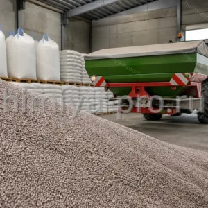 Приллированные серо-розовые гранулы азофоски 16-16-16 насыпью у разбрасывателя на складе зернового хозяйства.