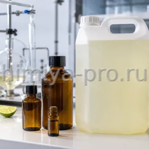 Бледно-жёлтое дистиллированное эфирное масло лайма во флаконах и канистре на белом лабораторном столе